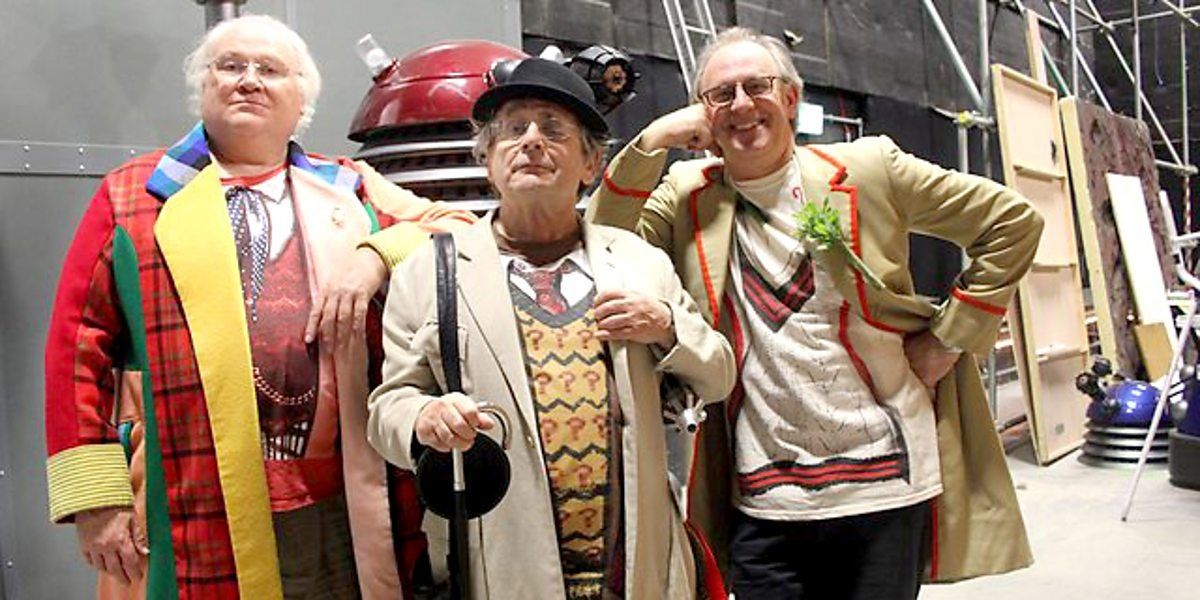 The Fifth, Sixth and Seventh Doctors pose in front of a Dalek.