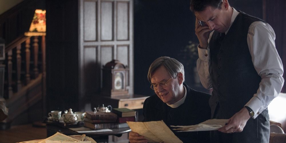An image of Frank and Reverend Wakefield looking at some sheets in Outlander