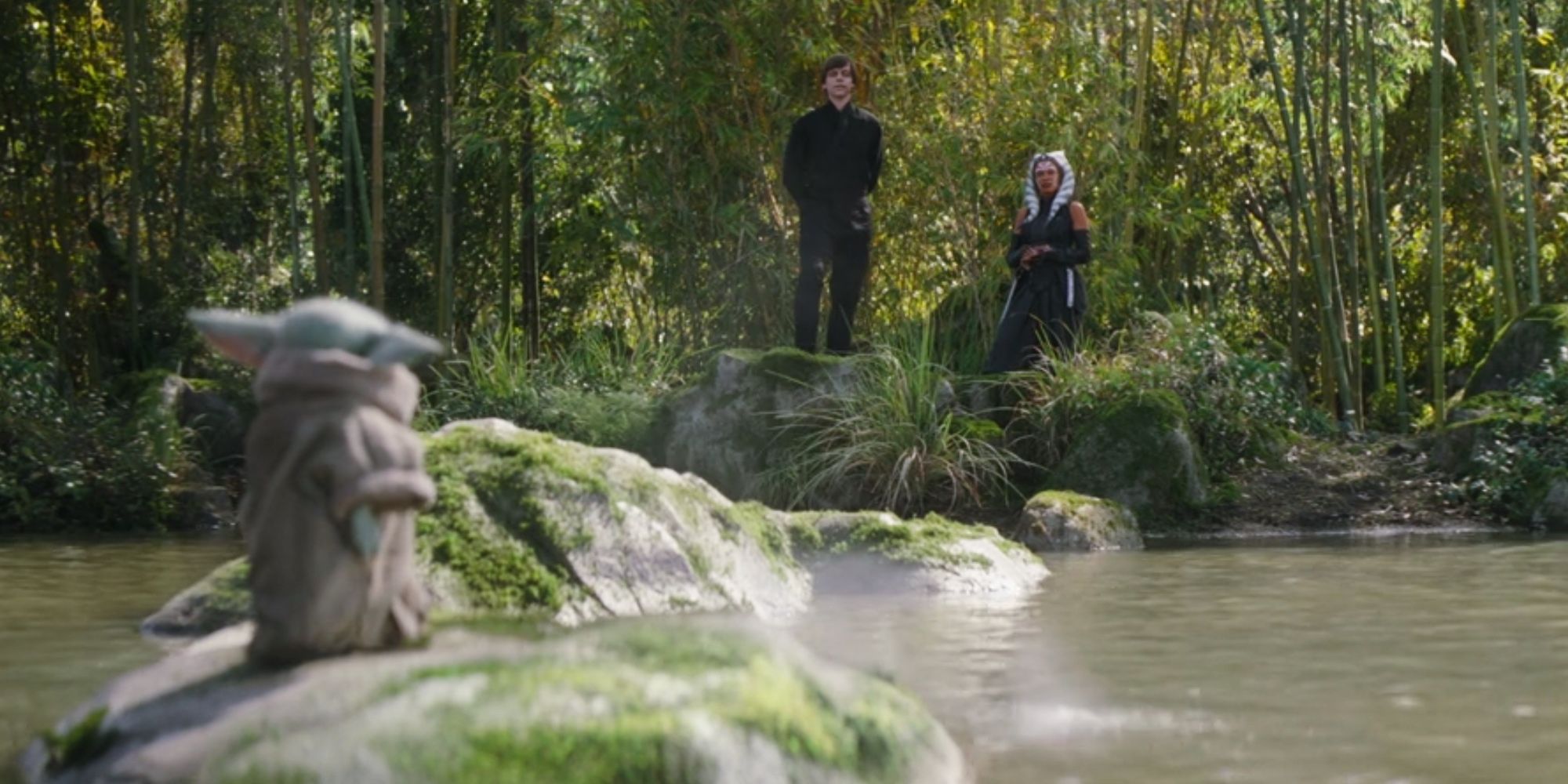 Grogu standing on a rock in a river in front of Luke Skywalker and Ahsoka