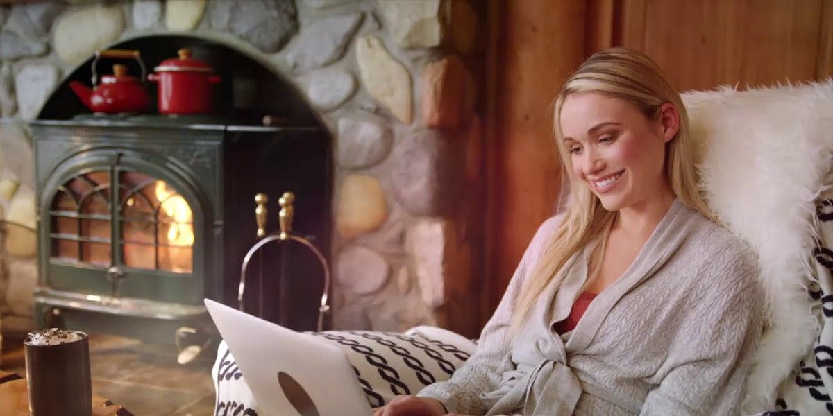 Girl sitting by the fireplace and smiling on her laptop in Love on the Slopes.