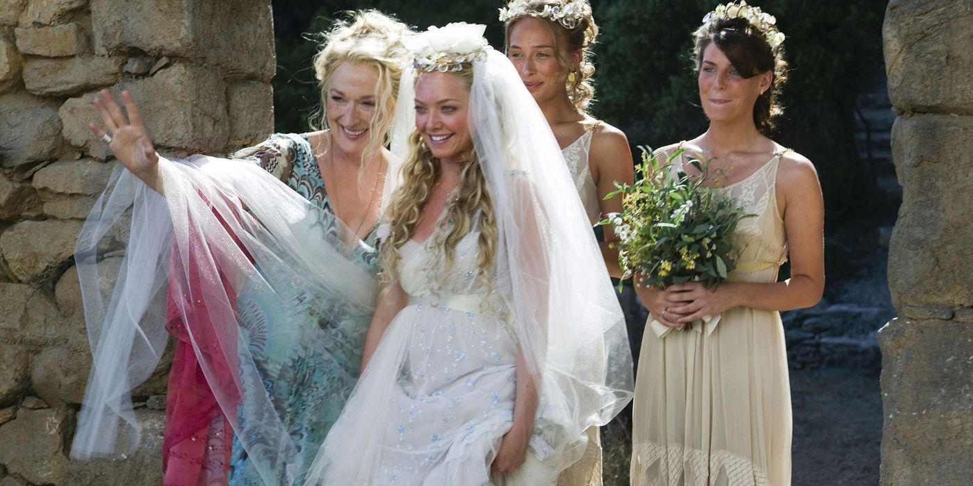 Amanda Seyfried's character about to walk down the aisle at her wedding with friends and mother in Mamma Mia