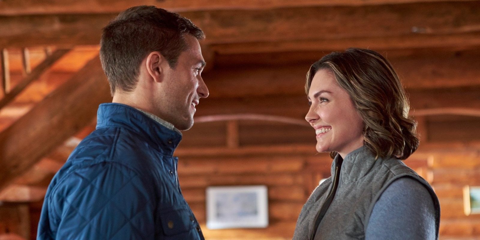 Ben and Cara smiling in a log cabin in One Winter Proposal