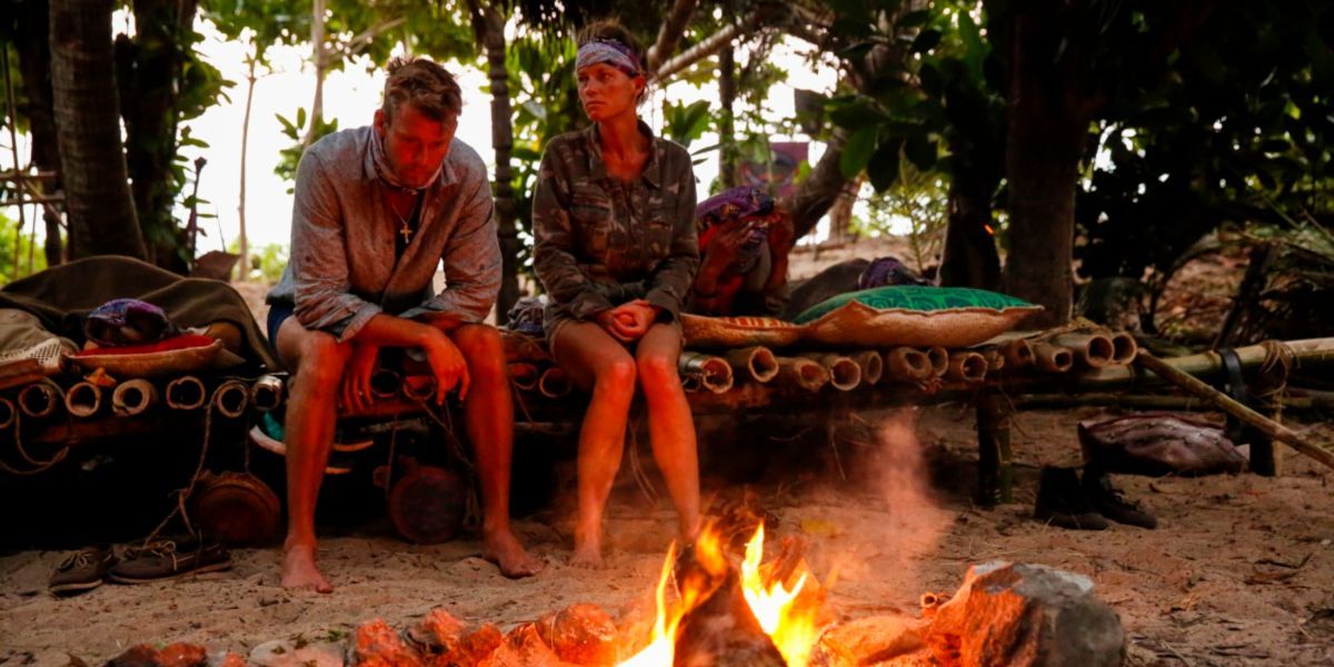 Dois competidores sentam-se ao lado de uma fogueira no Survivor