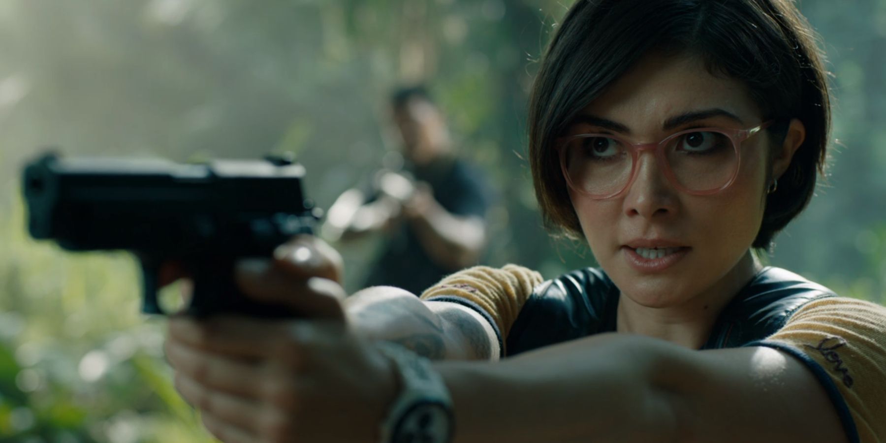 Zia Rodriguez aiming a pistol as Ken Wheatley in Jurassic World Fallen Kingdom