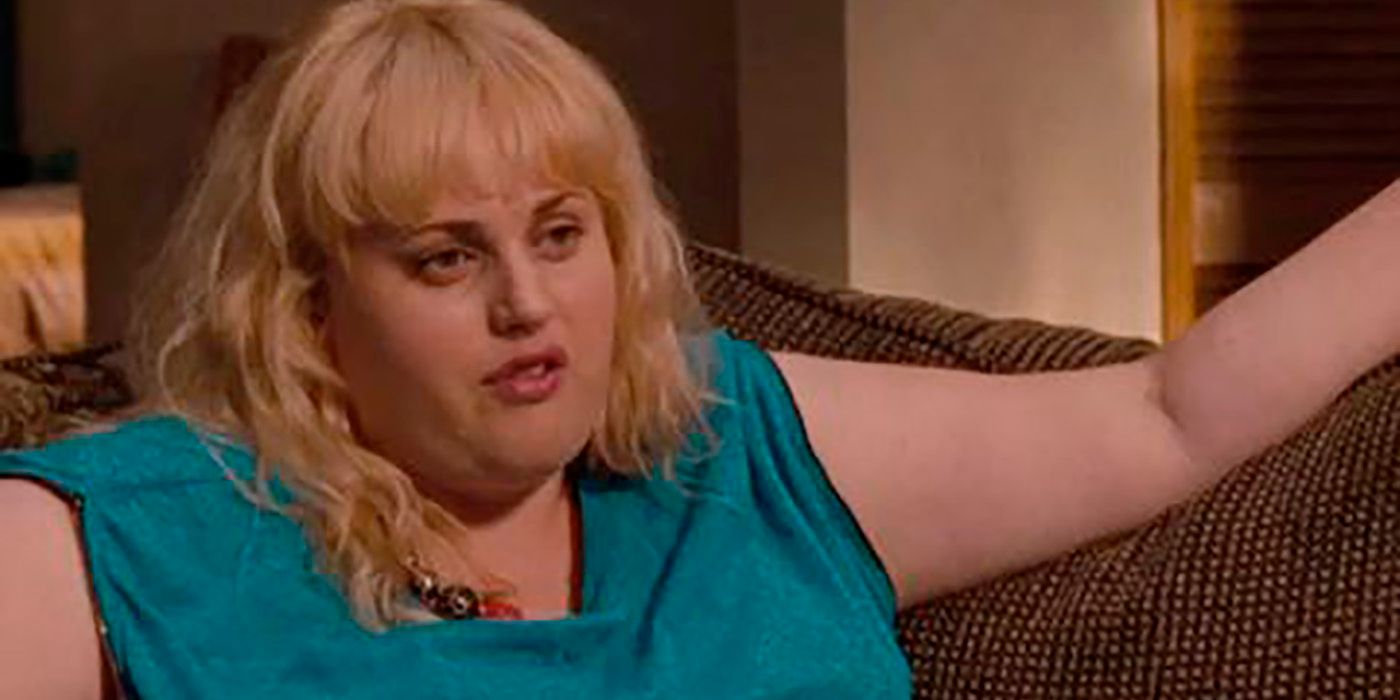 Rebel Wilson in green, sitting on a couch in a scene from Bridesmaids.