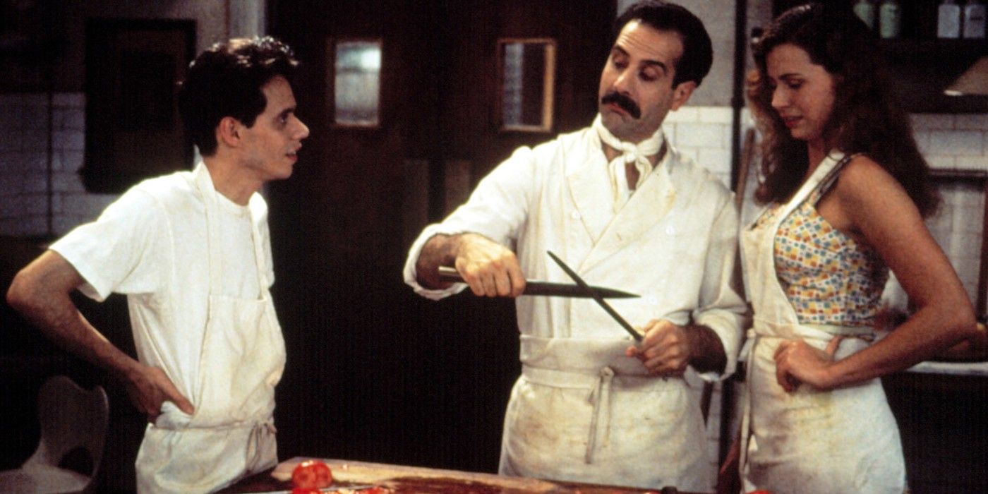 A man holds knives in a kitchen alongside his chefs in Big Night