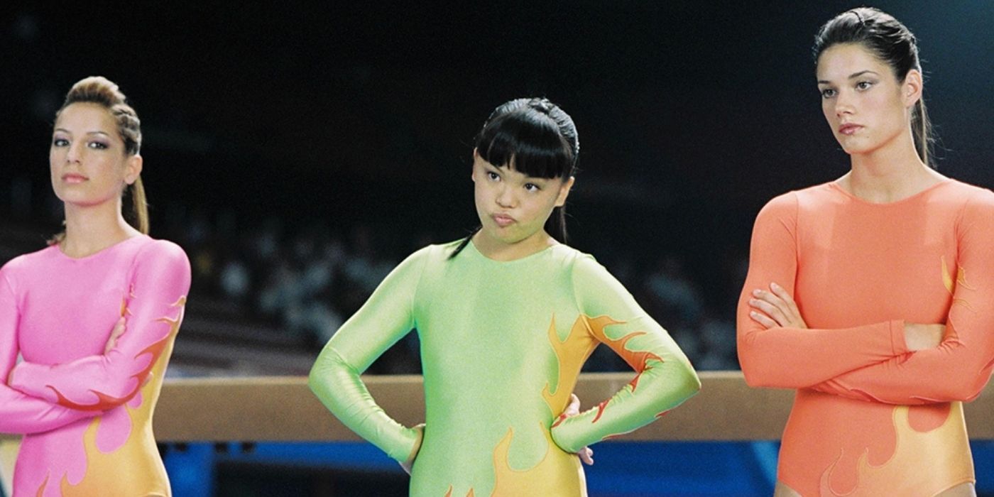 Haley, Wei Wei, and Joanne in leotards, crossing their arms and watching their competition at the gymnastics