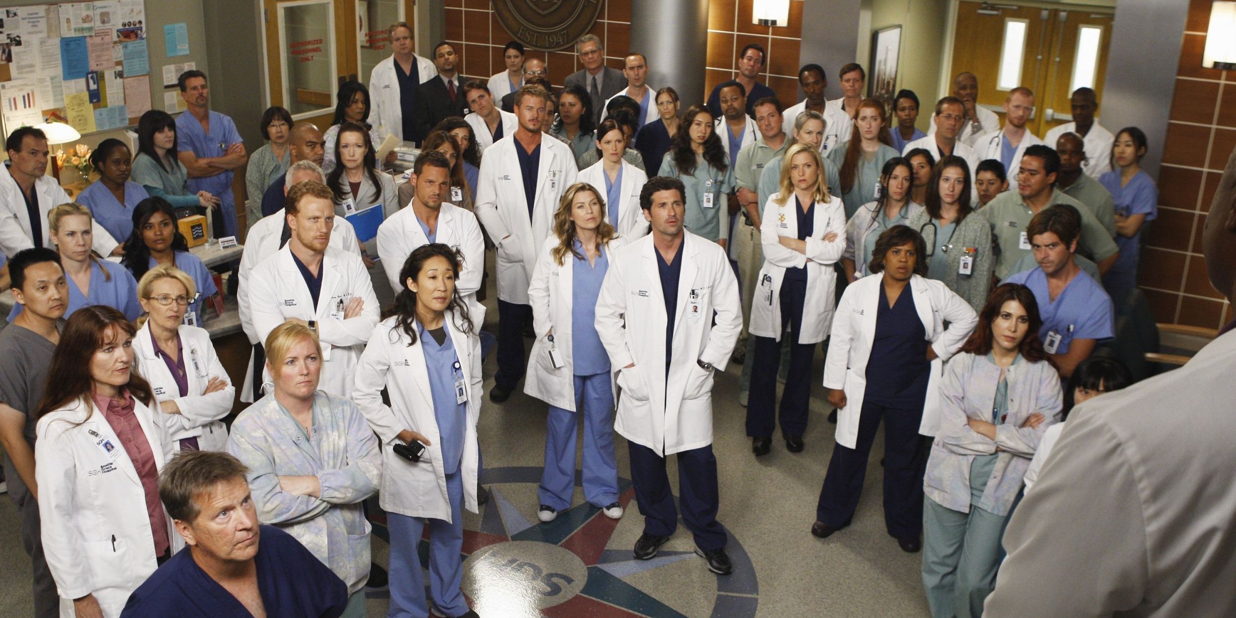 Hospital doctors stand around listening to an announcement in Grey's Anatomy 