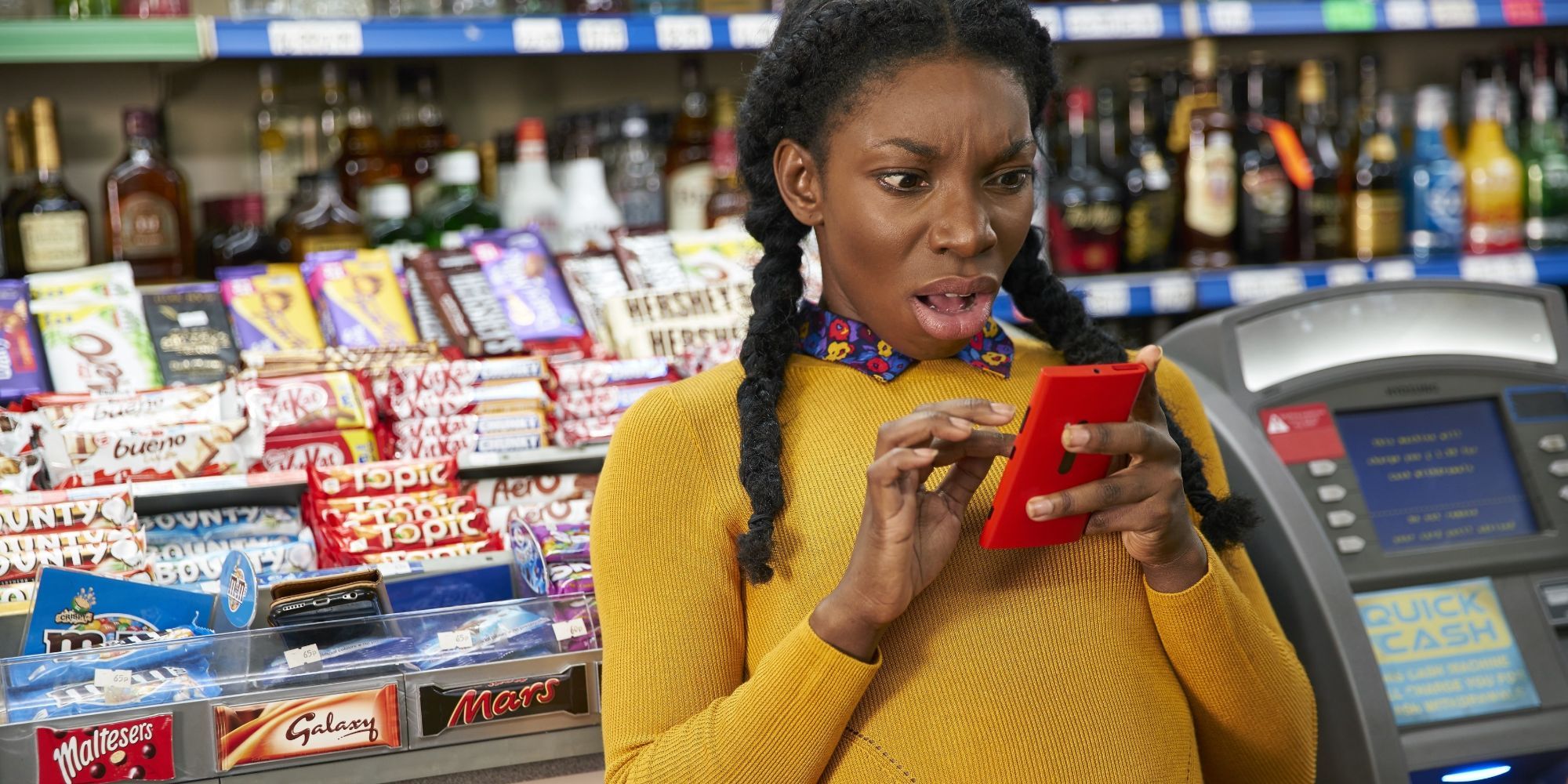 Michaela Coel in her sitcom Chewing Gum looking at the phone in her hand with a surprised expression