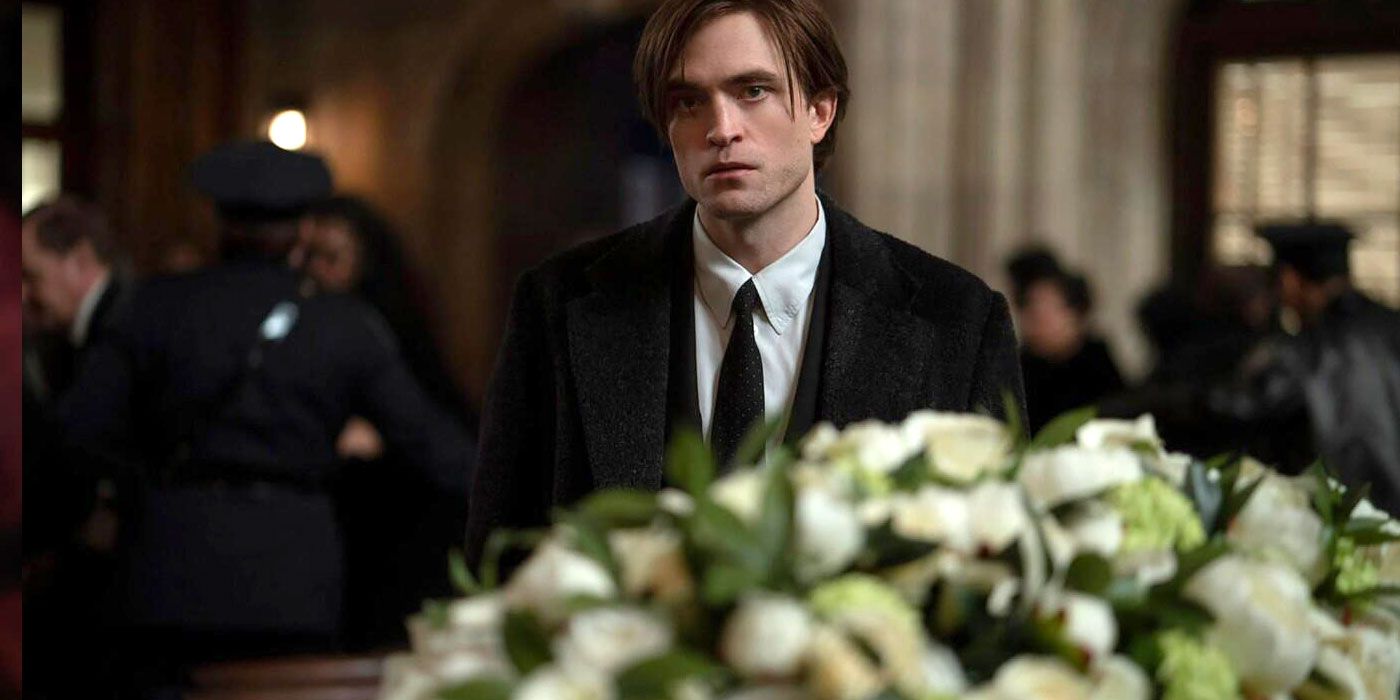 Bruce Wayne, standing near a funeral bouquet of white flowers.