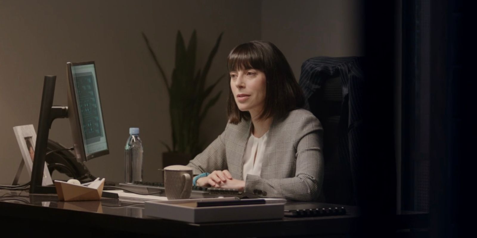 Lucy sitting at her desk on her computer in a scene from Upload.