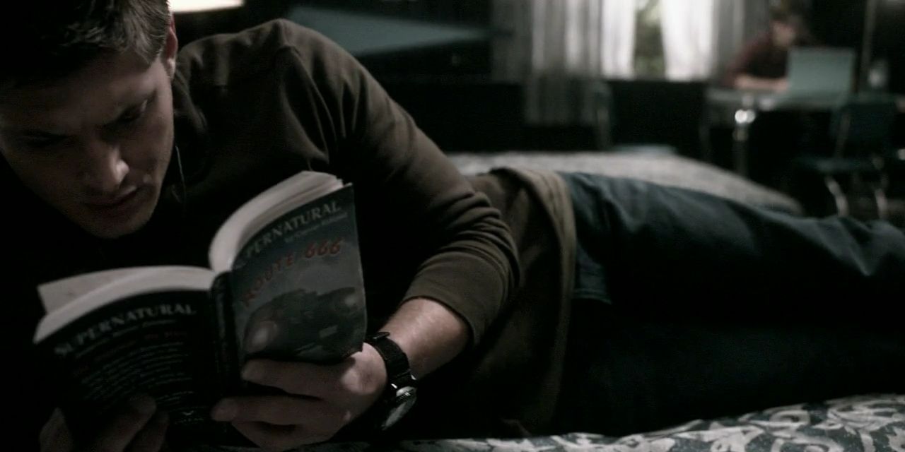 Dean Winchester on a bed reading Chuck&rsquo;s Supernatural book Route 666