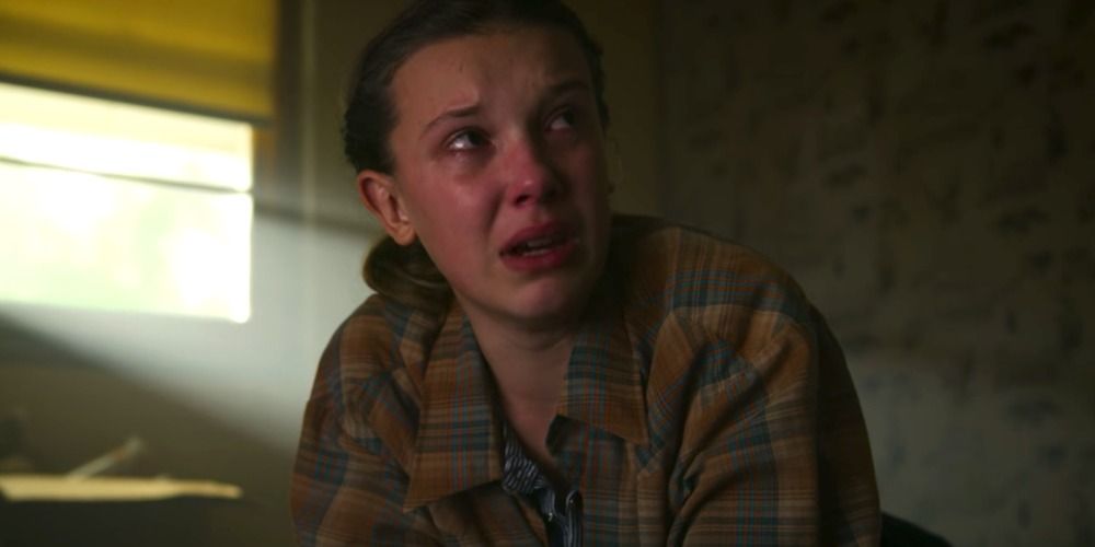 An image of Eleven crying while wearing Hopper's shirt in Stranger Things