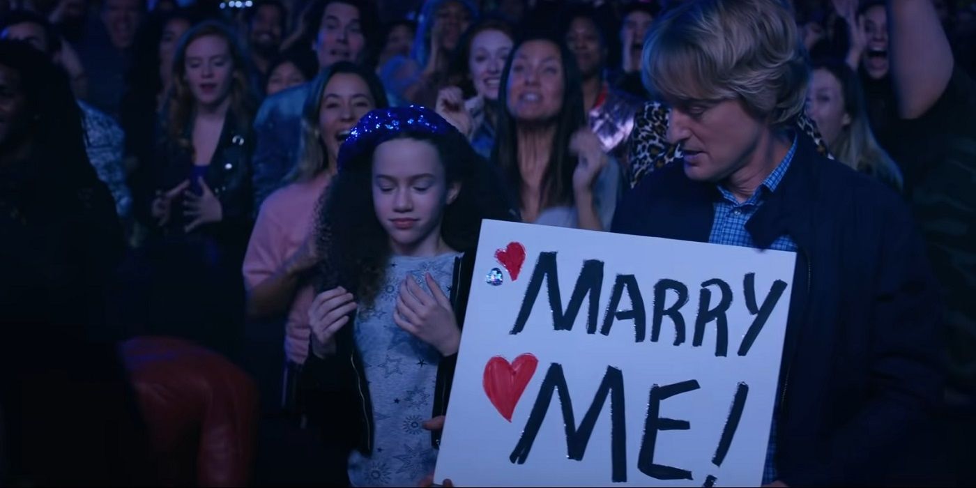 Owen Wilson holding a sign saying &quot;marry me&quot; in Marry Me