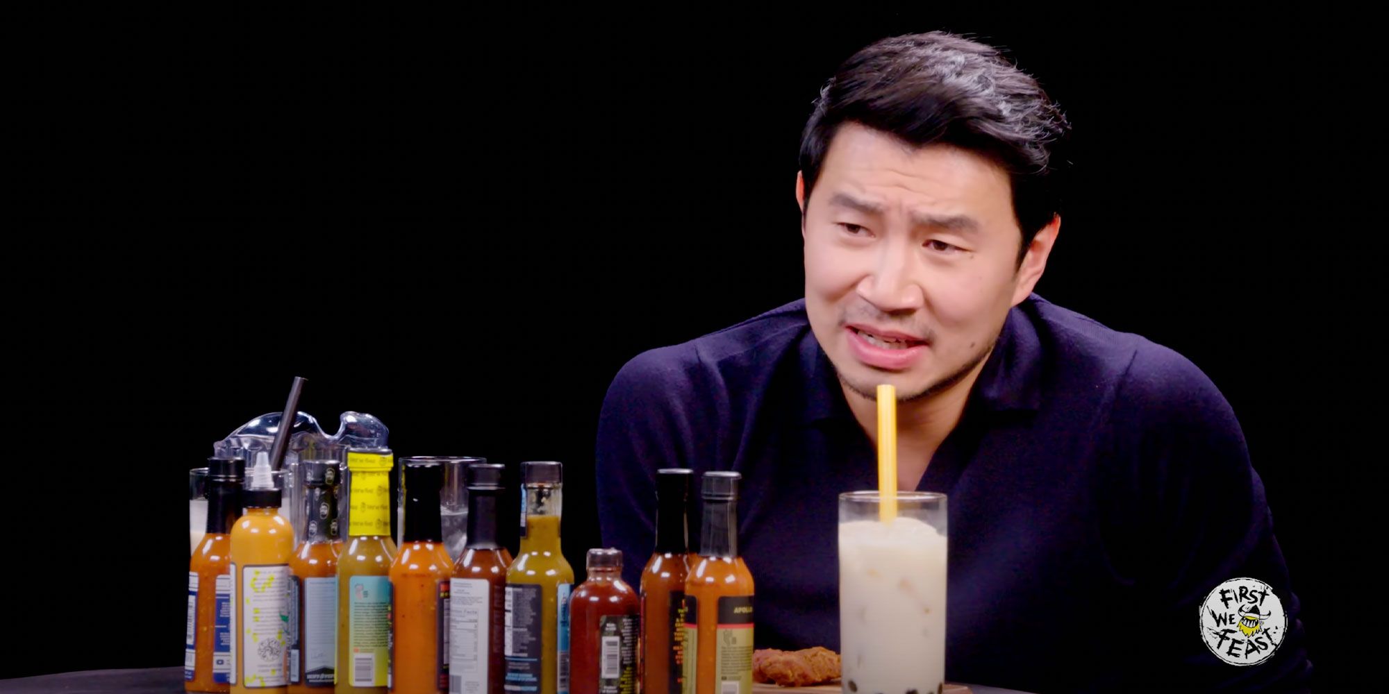 Simu Liu with hot sauces and a glass of milk on Hot Ones