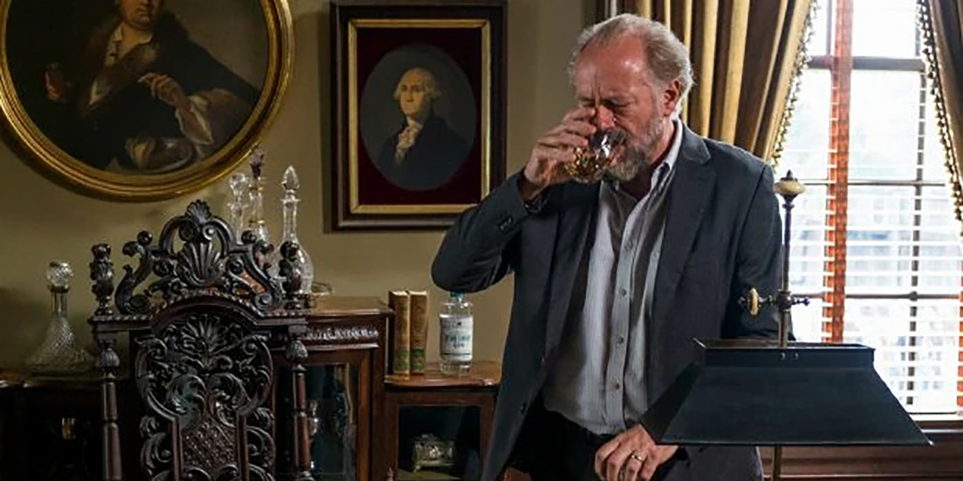Gregory from The Walking Dead standing in his office, drinking whiskey.