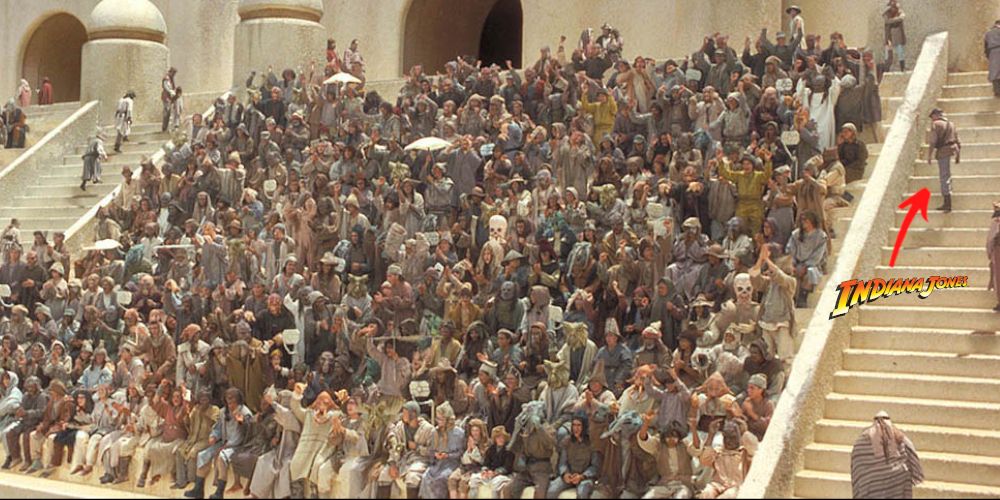 A character dressed similarly to indiana jones walks up the steps at the boonta eve podcast in star wars episode 1 the phantom menace while a huge crowd of characters watch the pod race