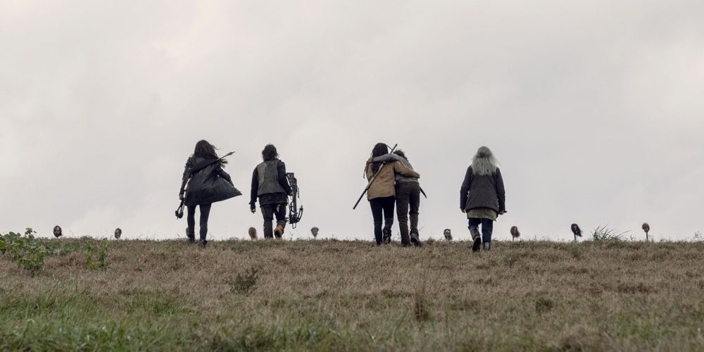 Characters walking toward heads on pikes in The Walking Dead 