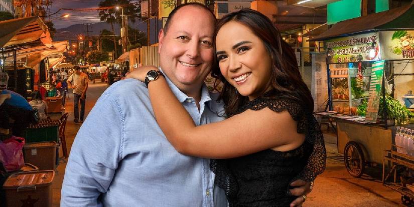 David Toborowsky wearing blue shirt and Annie Suwan in black dress in 90 Day Fiance hugging with Thailand market in the background