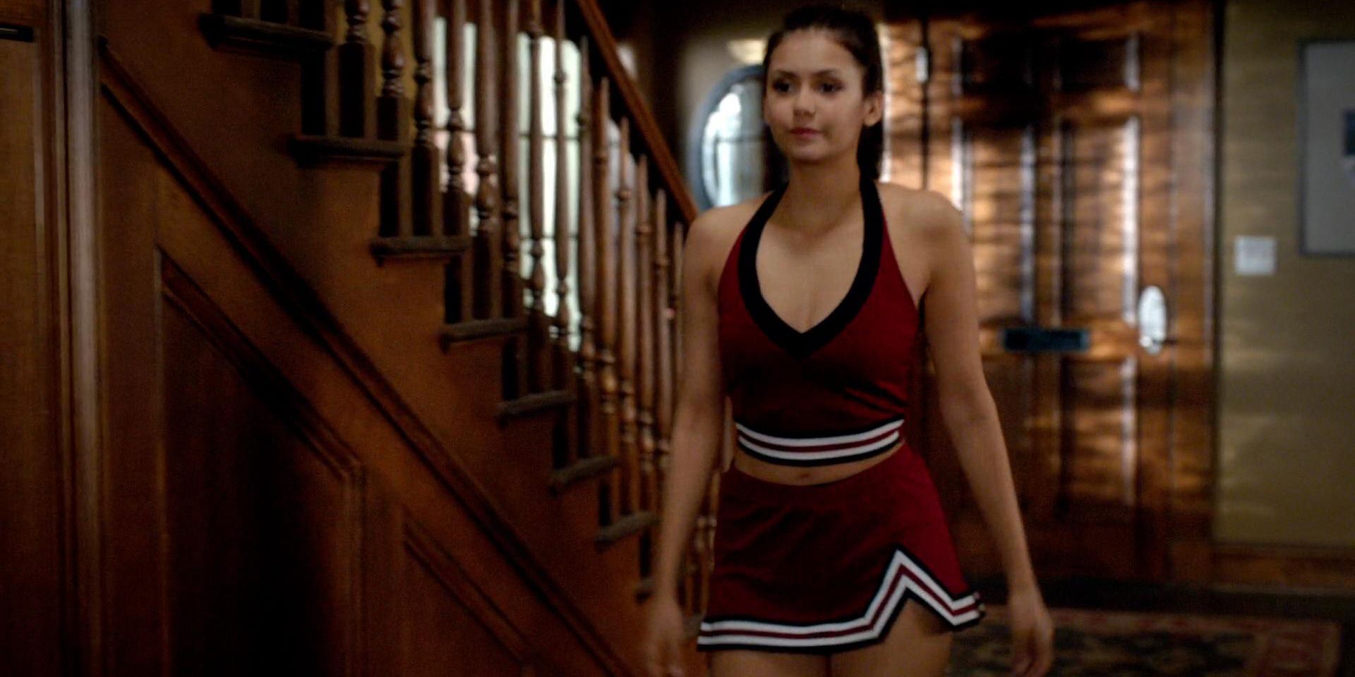 Elena Gilbert em seu traje de líder de torcida em The Vampire Diaries descendo as escadas parecendo séria.