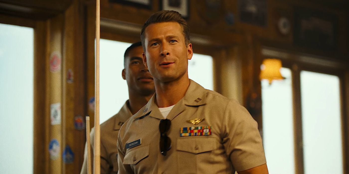 Glen Powell in character as Hangman in Top Gun: Maverick wearing a military uniform and holding a pool cue