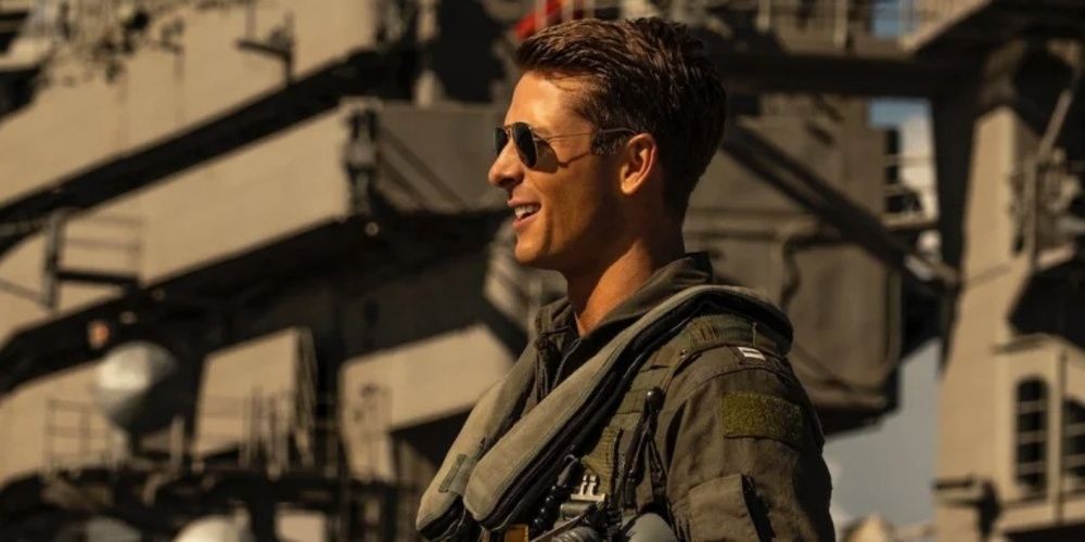 Hangman wearing shades and smiling while standing on the deck of a ship in Top Gun Maverick 