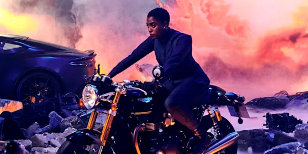 Lashana Lynch as Nomi 007 on a motorcycle surrounded by explosions, rubble and the aston martin for no time to die publicity