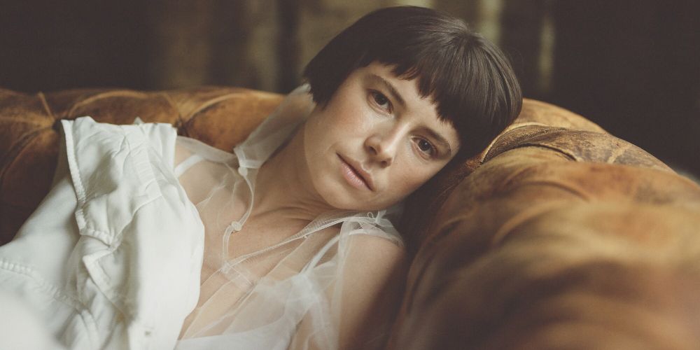 Leda lays on the sofa in a white blouse in The Lost Daughter