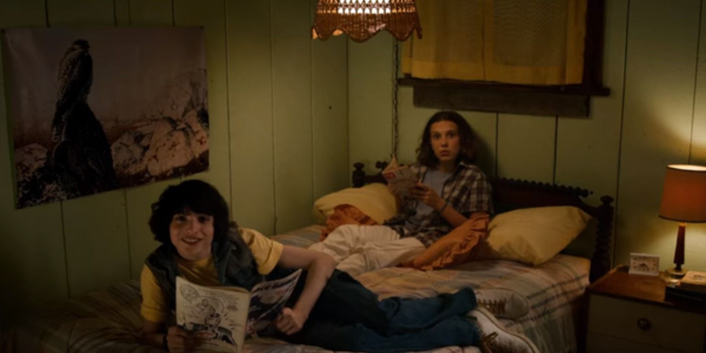 Mike Wheeler lying on Eleven's bed with a bird poster above his head with Eleven sitting behind him on Stranger Things