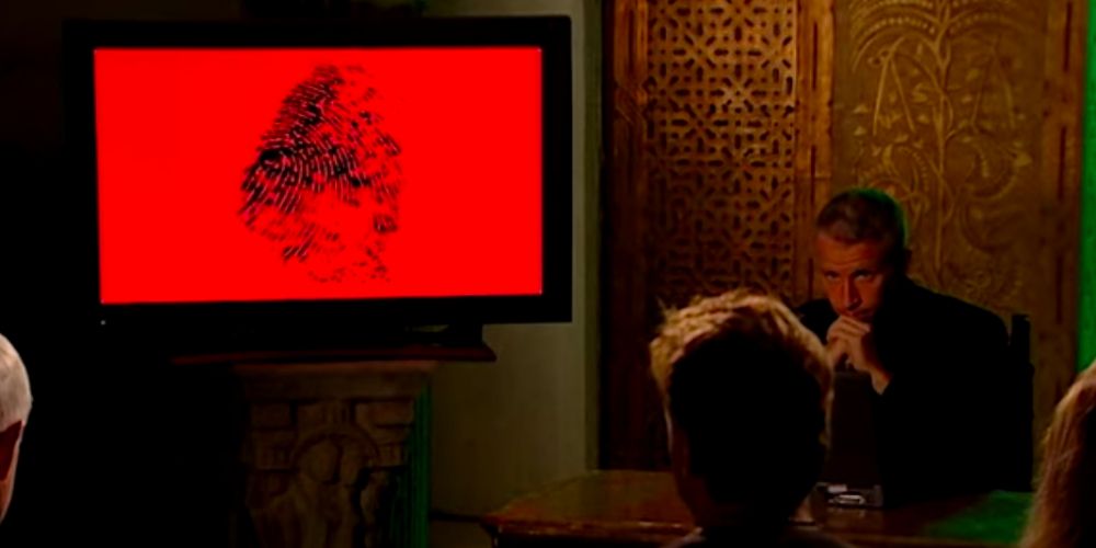 Anderson sits by the red quiz screen on The Mole