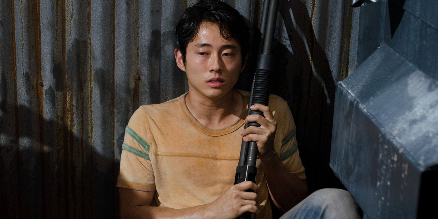 Glenn from The Walking Dead sitting on the floor holding a rifle.