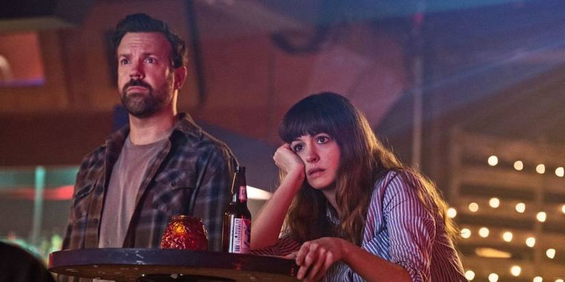 Anne Hathaway and Jason Sudeikis staring at the TV with serious expressions in Colossal