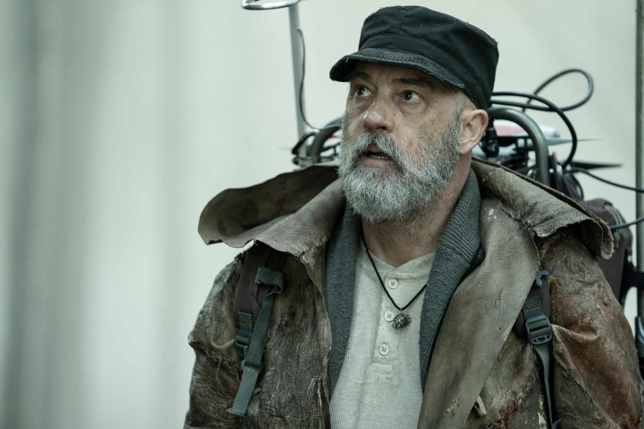 Anthony Edwards in character in Tales of the Walking Dead with a gray beard and cap wearing a contraption on his back