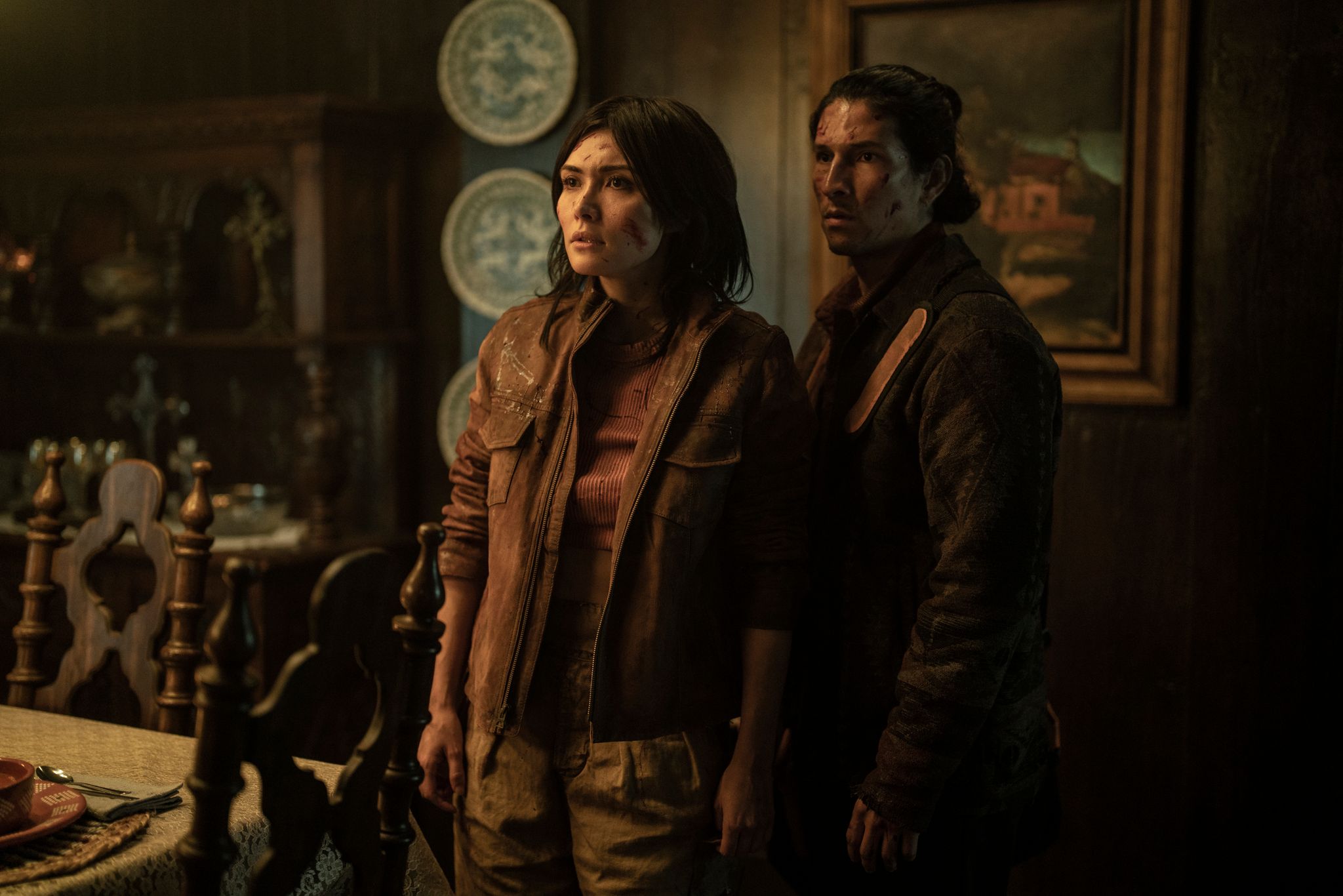 Daniella Pineda as Idalia and Danny Ramirez as Eric in character in Tales of the Walking Dead standing in a fancy-looking dining room