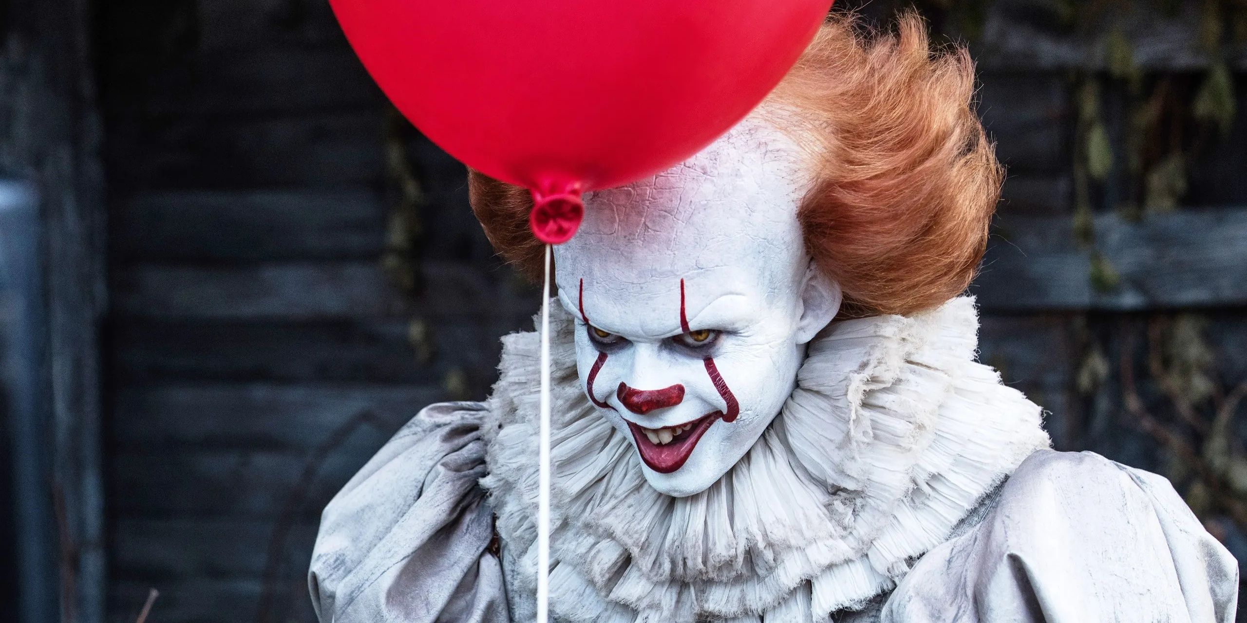 Pennywise smiling while holding a red balloon