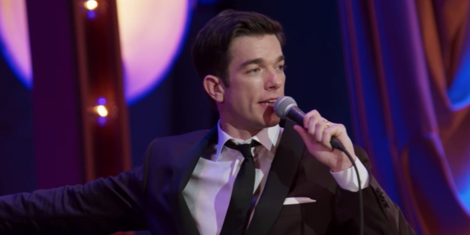 John Mulaney points behind him while speaking into a microphone at Radio City Music hall