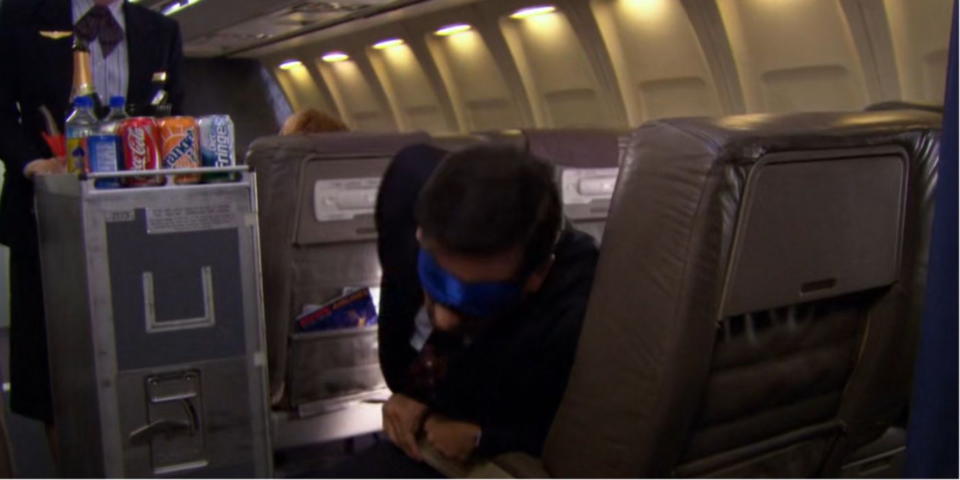 Michael Scott shrieks from pain as the flight attendant stands near him with a service trolley in The Office