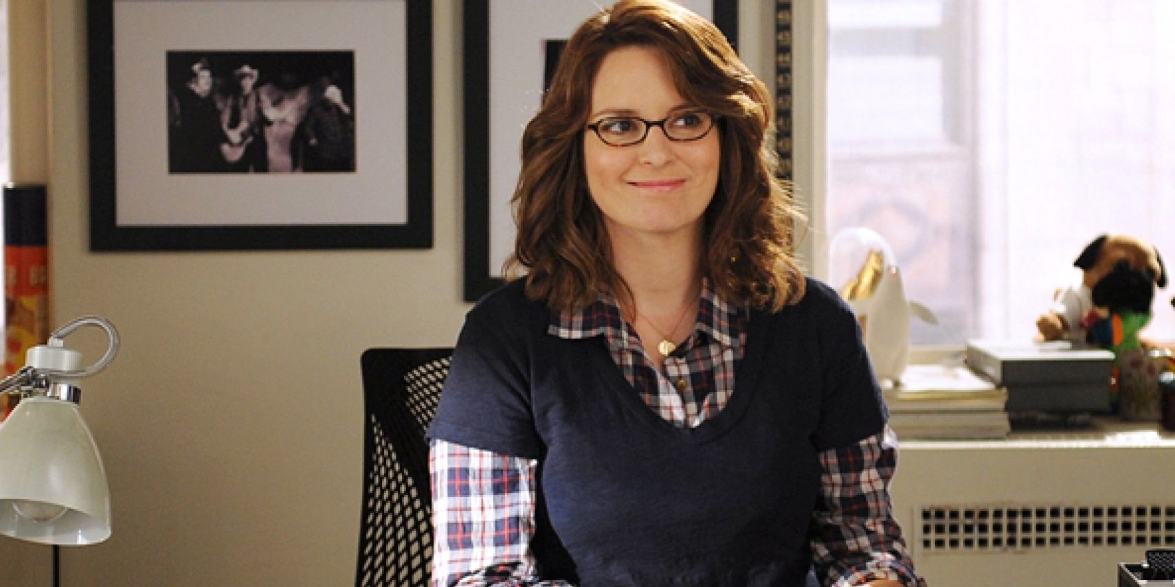 Tina Fey sitting at a desk and smiling in 30 Rock