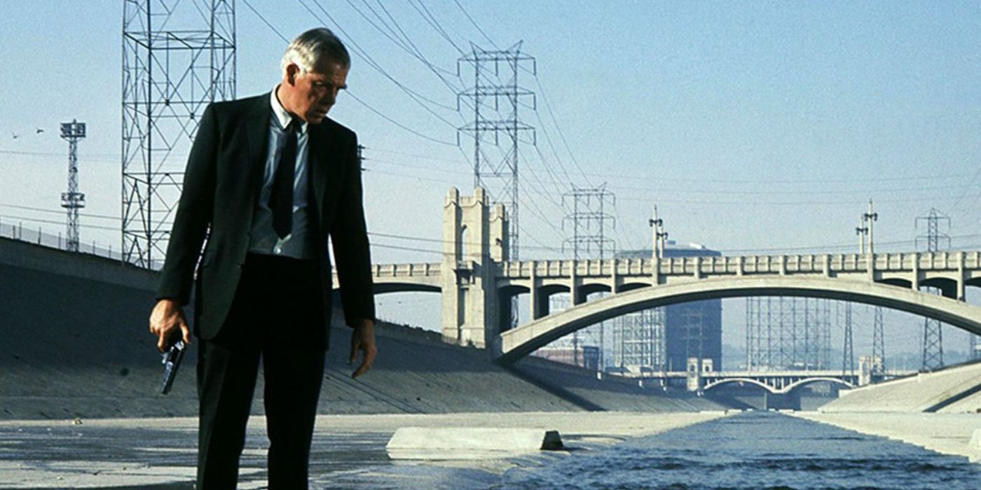 Lee Marvin wearing a suit holding a gun in an urban river in Point Blank
