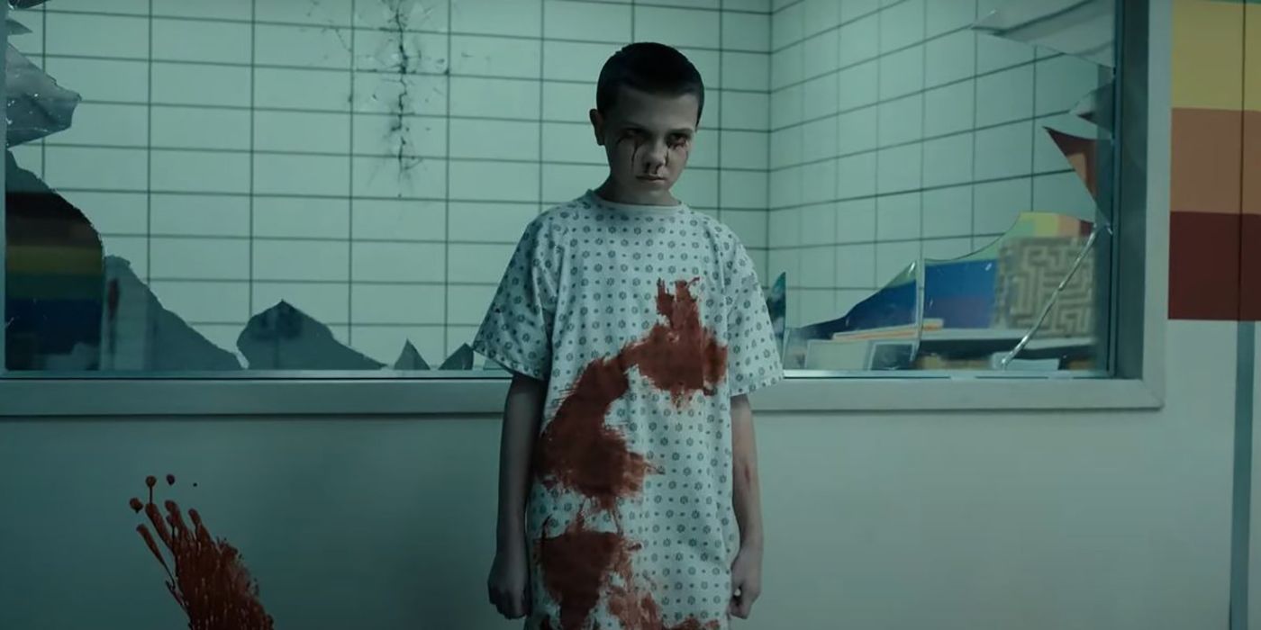 A young Eleven in the lab in Stranger Things, blood on her clothing and face.