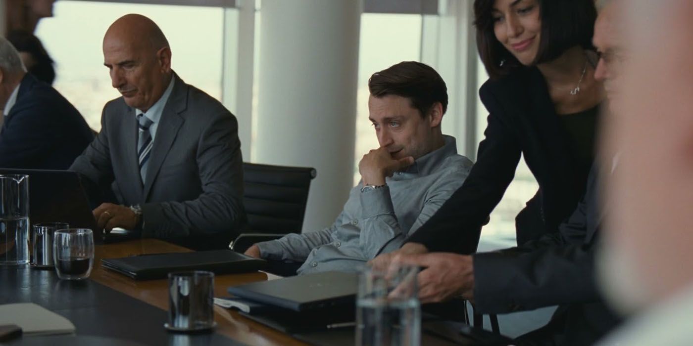 Roman from Succession sitting in a boardroom looking mischievously 