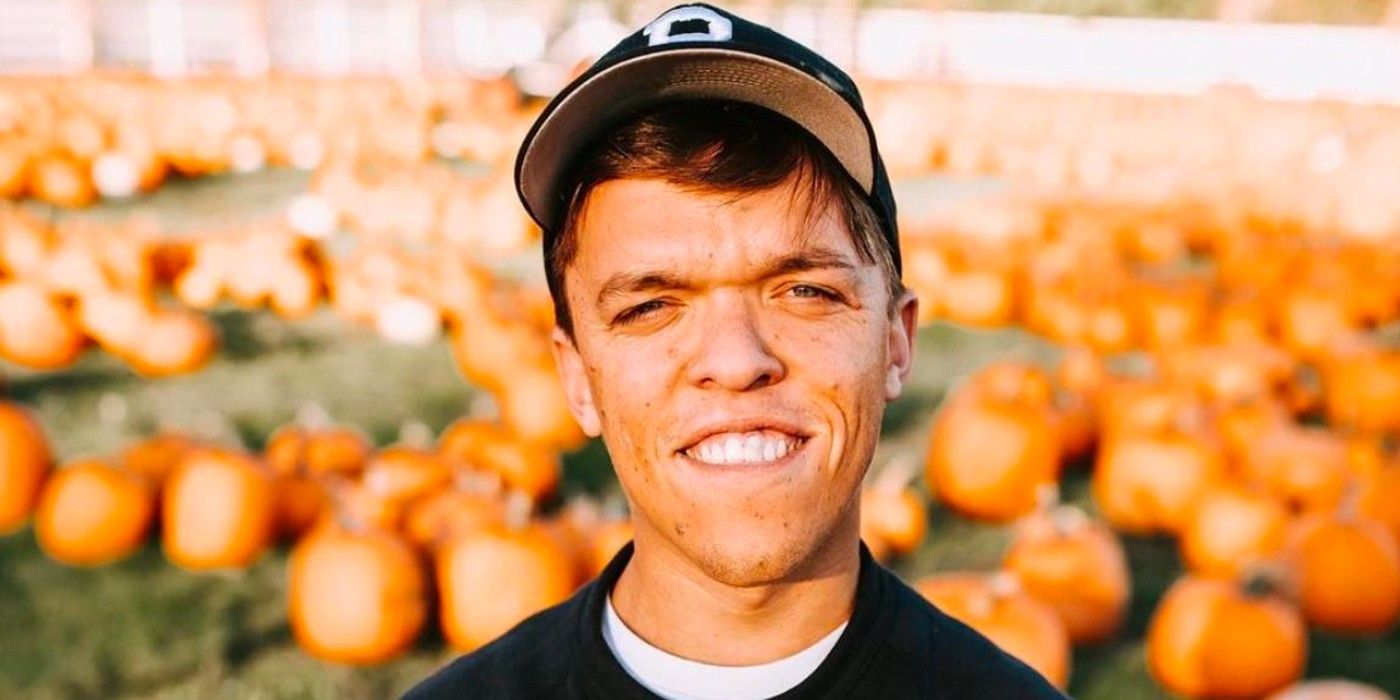 Little People, Big World star Zach Roloff with a pumpkin patch behind him smiling with a hat on