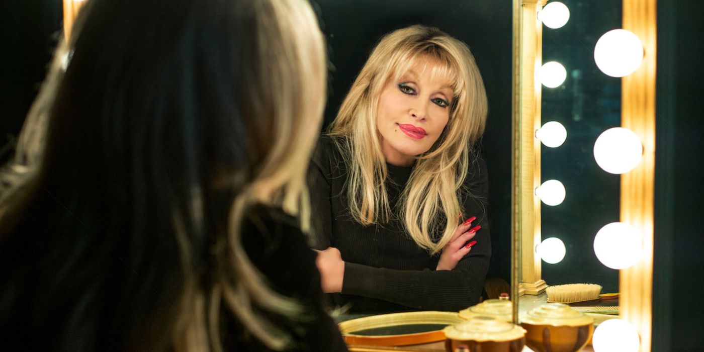 Dolly Parton looking at her reflection in a light-up vanity mirror.