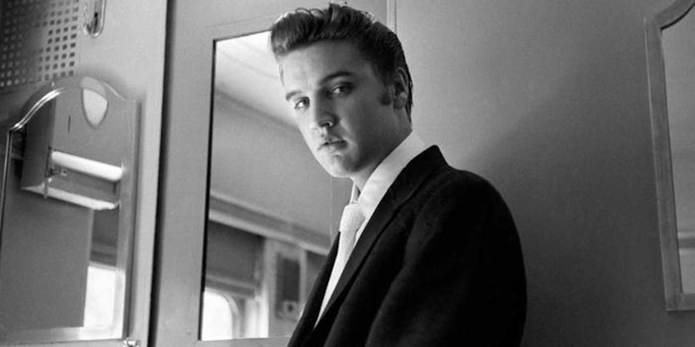 Black-and-white photograph of Elvis Presley looking down at the camera in a dressing room