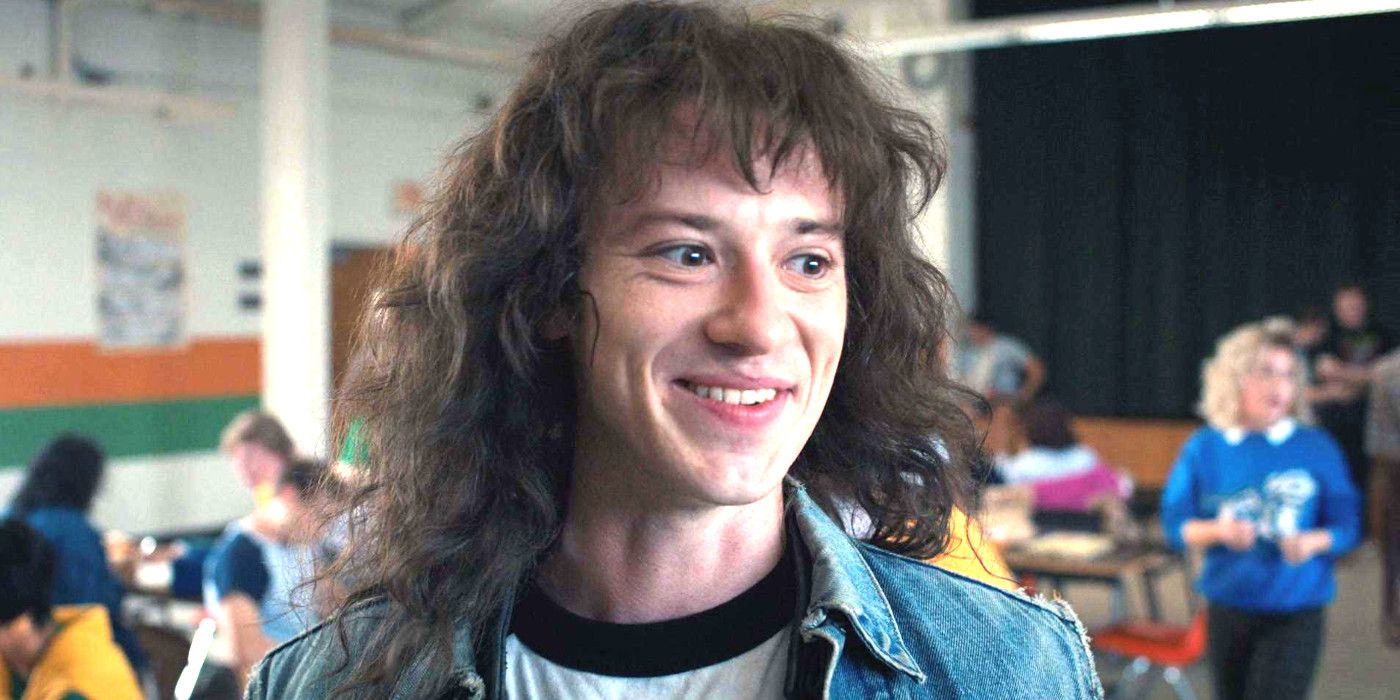 Joseph Quinn as Eddie Munson in Stranger Things in a cafeteria smiling somewhat maniacally
