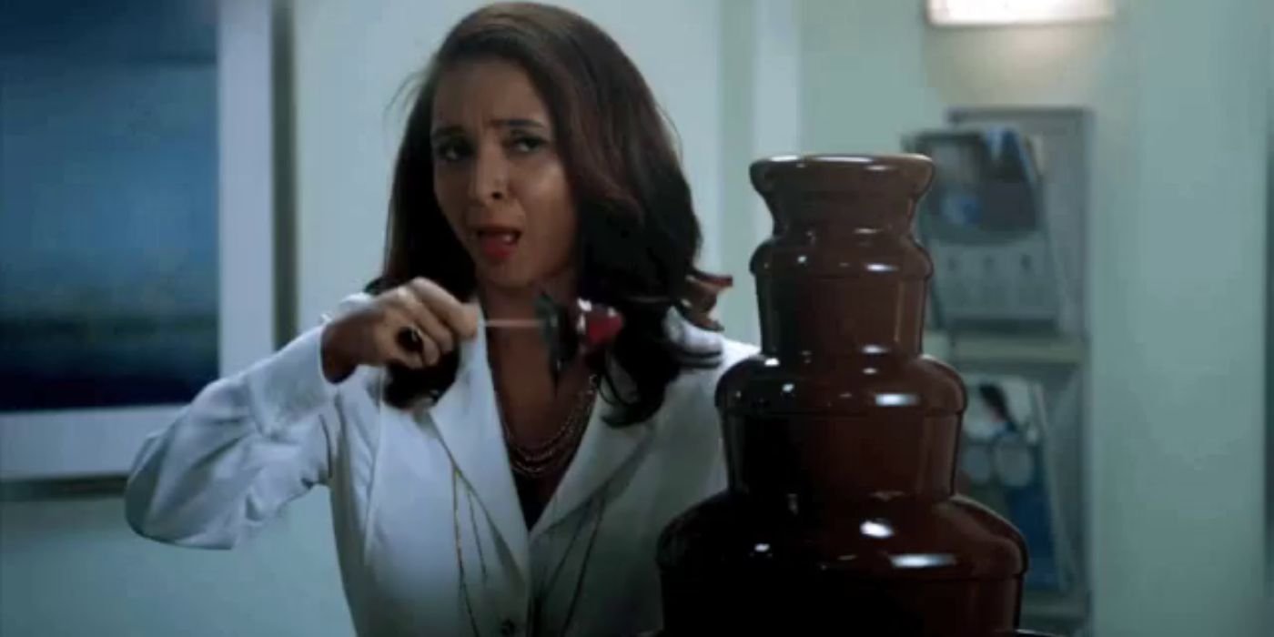 Jackie dipping a strawberry in a chocolate fountain in Angie Tribeca.