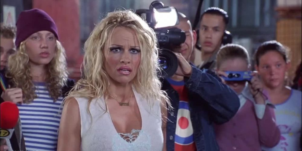 Pamela Anderson stands in front of a crowd, shocked to learn who the bad guy is