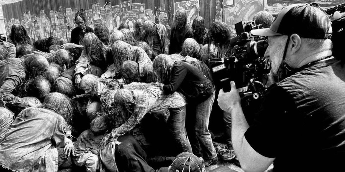 A camera operator films the action as extras in zombie makeup attack a person lying face down on the ground.