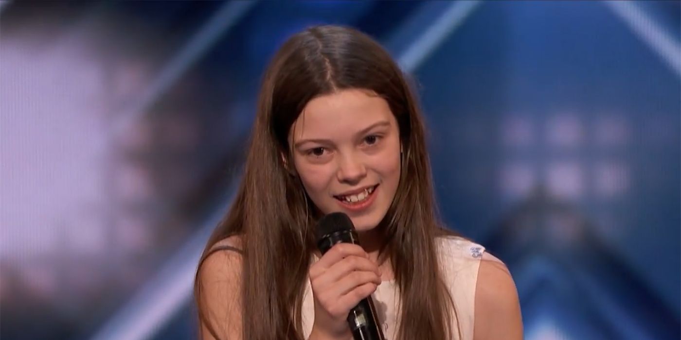 Courtney Hadwin on the AGT stage smiling, mic in her band.