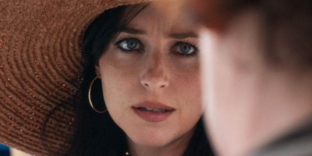 Nina frowns in a sun hat in The Lost Daughter